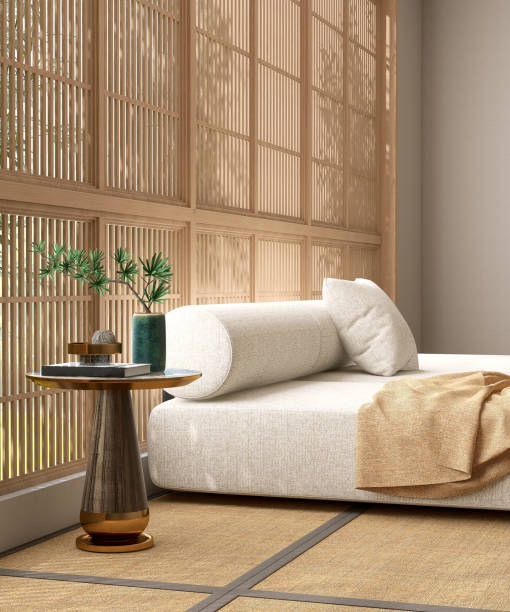 Gold brown steel round side table by modern white fabric bolster cushion back sofa in sunlight from wooden shoji window, Japanese tatami mat
