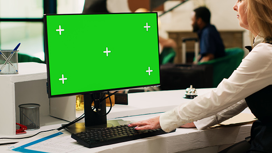 Receptionist using greenscreen pc at front desk lobby, looking at isolated display with chroma key template. Hotel concierge at reception checking mockup copyspace on computer.