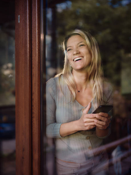 istock Happy woman using mobile phone by the window at home. 1494741035