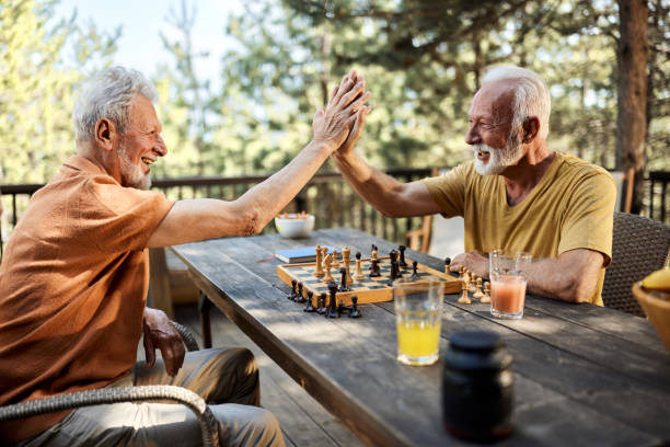Give me high-five, great game! Happy mature man congratulating his friend on successful chess game on a terrace. senior chess stock pictures, royalty-free photos & images