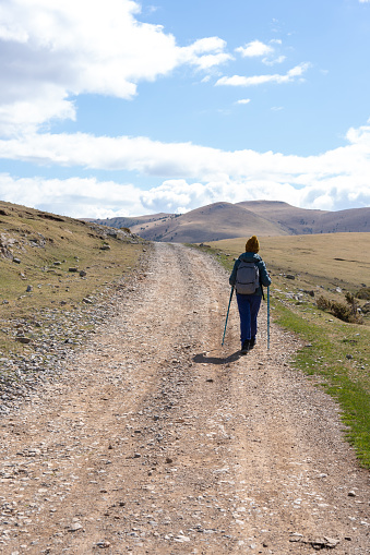 Single woman walking with sticks and backpack enjoying a day trekking in a sunny day of spring