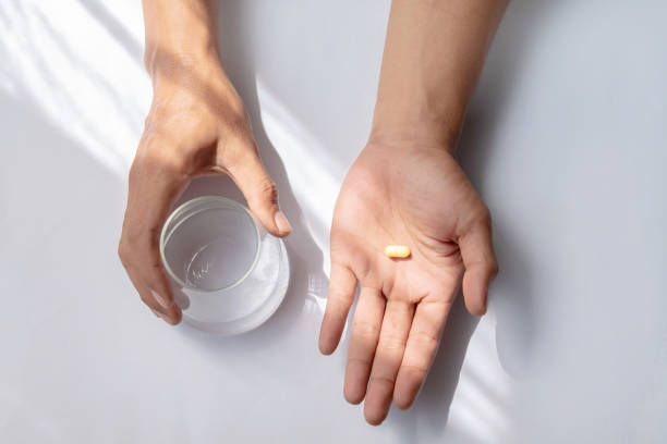 uomo asiatico che tiene pillole e un bicchiere d'acqua - painkiller pill capsule birth control pill foto e immagini stock
