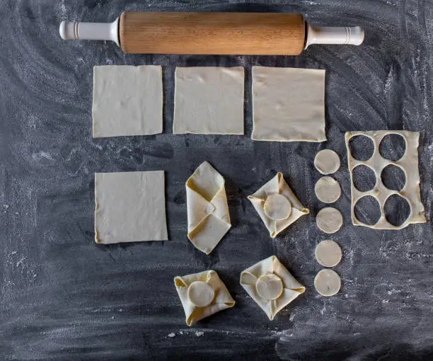Forming, folding and shaping raw puff pastry dough. Flat lay on dark background with rolling pin.