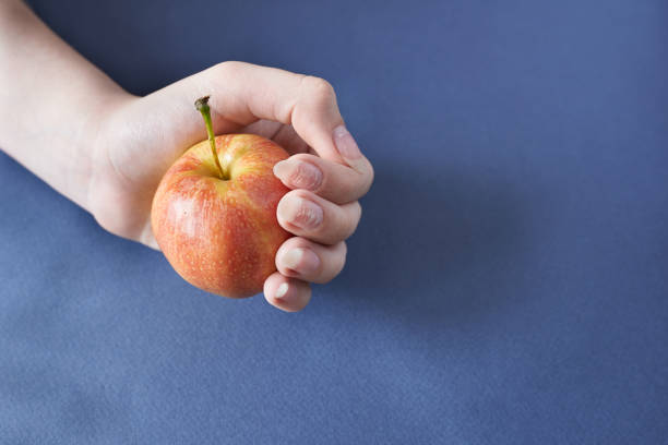 istock Female hand holding a fresh red apple on blue background with copy space 1494744837