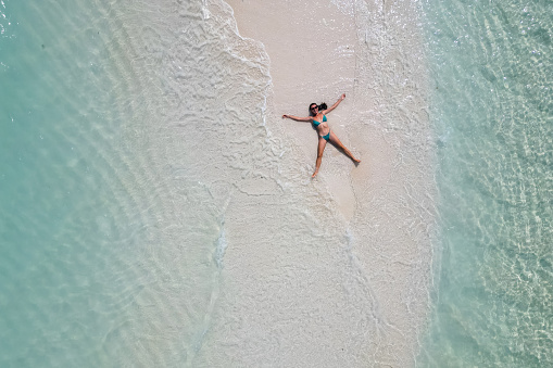 young woman tanning sunbathing woman wearing bikini at the beach on a white sand from above view from drone.