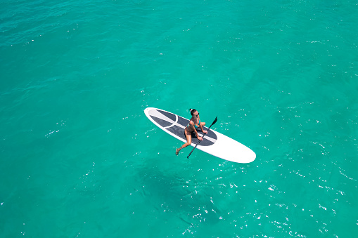 Aerial view of a woman on a white supboard in the turquoise waters of the Maldives.