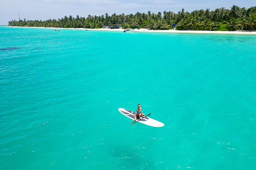 Aerial view of a woman on a white supboard in the turquoise waters of the Maldives.