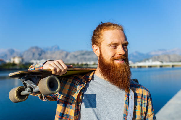 istock handsome redhaired man with long beard skateboarding near river at sunny summer day 1494746601