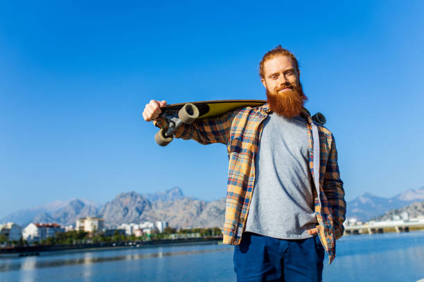 istock handsome redhaired man with long beard skateboarding near river at sunny summer day 1494746606