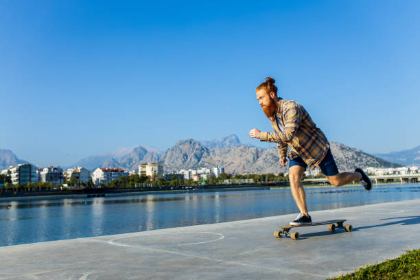 istock handsome redhaired man with long beard skateboarding near river at sunny summer day 1494746609