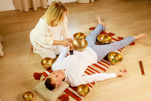 Woman playing on a tibetian singing bowl maling massage meditation for a man.