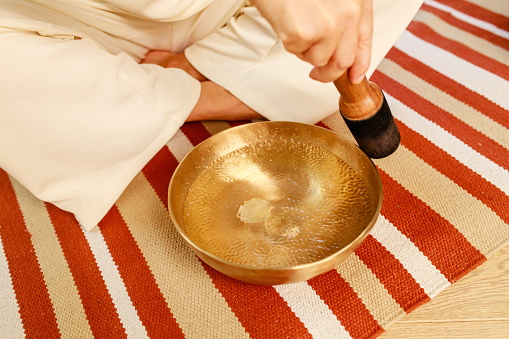 Woman playing on a tibetian singing bowl in cozy room meditating in a yoga.