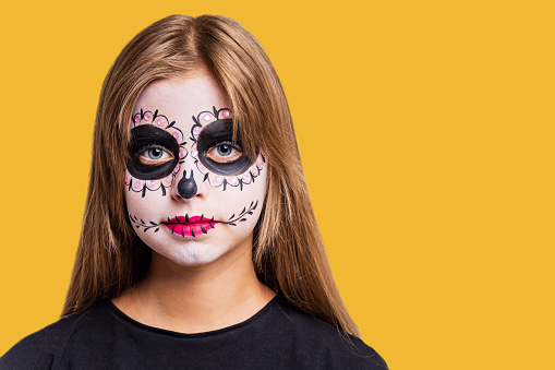 Portrait of young beautiful girl with make-up skeleton on her face in yellow studio background.