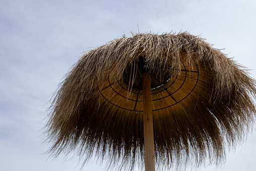 The top of a reed umbrella on the beach against a cloudy sky