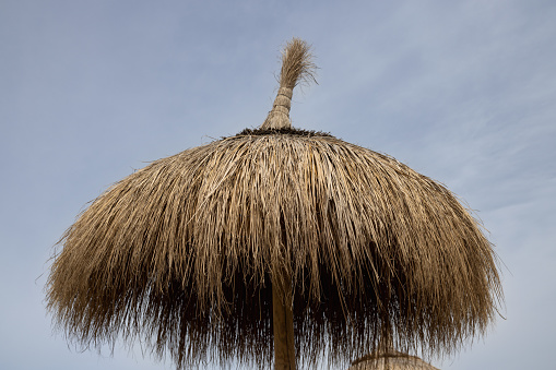 The top of a reed umbrella on the beach against a cloudy sky