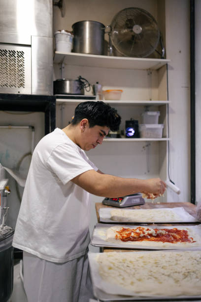 istock Young baker putting ingredients in pizza 1494751228