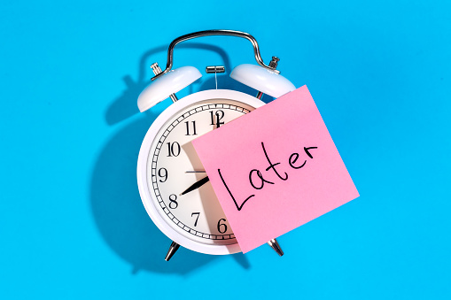 White alarm clock and sticker with the inscription Late on a blue background, flat lay.