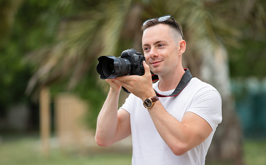 Man photographer take a photo at the summer park with palm tree on background