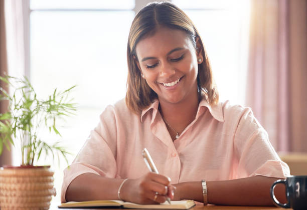 istock University, planning and woman student writing in a notebook working on a school project in her home. Education, happy and female college scholar from Mexico studying for a test or exam in apartment. 1494764800
