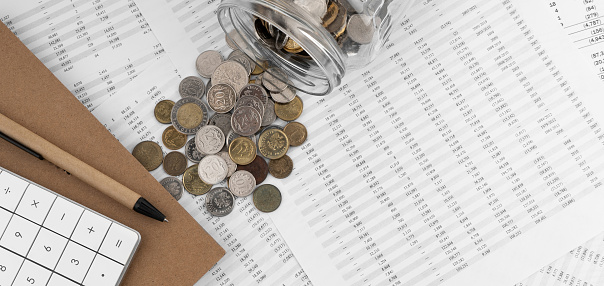 Calculator on financial statement and coins poured out of a glass jar.