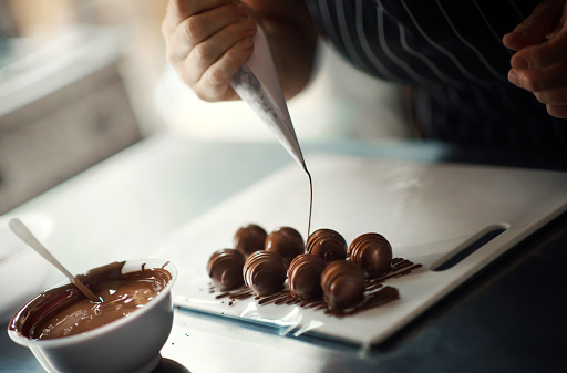 Closeup of a woman putting melted chocolate icing over chocolate truffles.