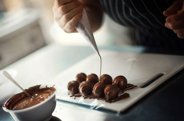 Decorating chocolate truffles. Closeup of a woman putting melted chocolate icing over chocolate truffles. chocolate truffle making stock pictures, royalty-free photos & images