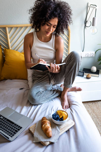istock Multiracial latina woman writing daily affirmations on journal while eating breakfast in bed next to laptop.Vertical. 1494767034