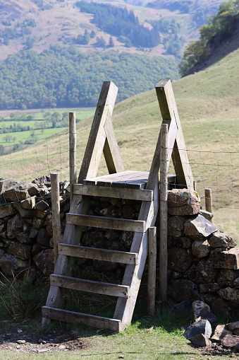 Wooden ladder stile on a footpath surrounded by rolling hills in sunshine