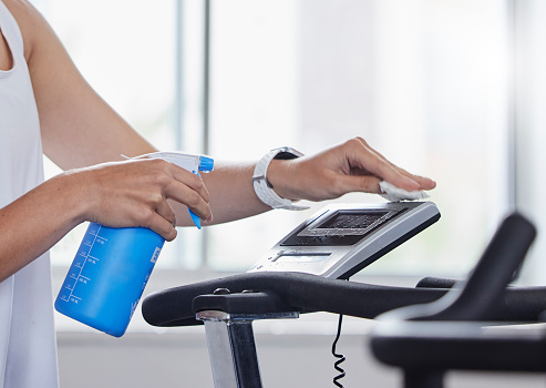 Sanitizer, disinfect and fitness person cleaning gym surface before exercise, workout and training for health and wellness. Hygiene, wipe and anti virus on a treadmill by hand spray equipment clean