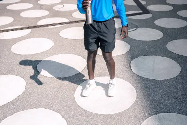 young sportsman standing on white circles at town square, holding water bottle