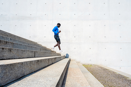 young sportsman running down steps in front of concrete wall outdoors in berlin at sunny day