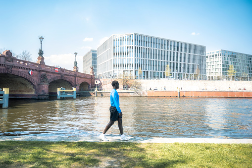 young black sportsman walking at river side in modern berlin at sunny day