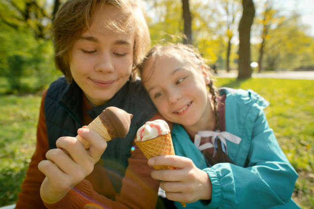 niños comiendo helado en un parque en verano o primavera - ice cream licking little boys ice cream cone fotografías e imágenes de stock
