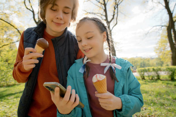 istock Children eating ice-cream and using smartphone in a summer park 1494775771