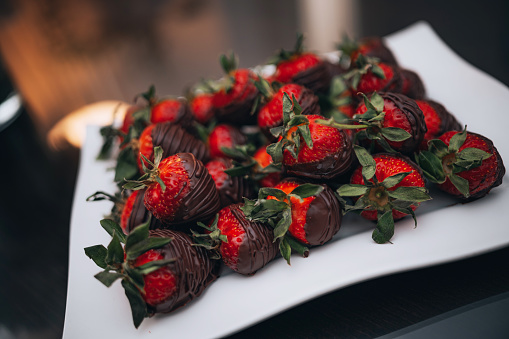 Close-up of fresh strawberries covered with dark chocolate on a white plate