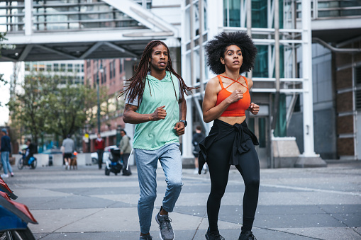 Sporty young couple running in the city of New York in the evening. Health and wellbeing concept, happy afro-american woman and man getting fit outdoors.