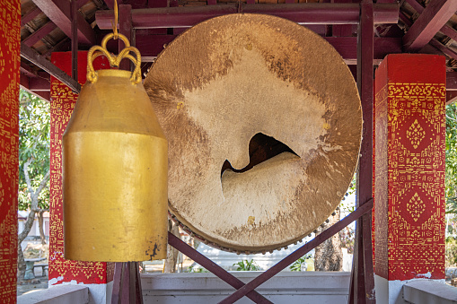 a photography of a bunch of bells hanging from a metal pole, bells hanging from a metal structure with a red roof and a blue sky.