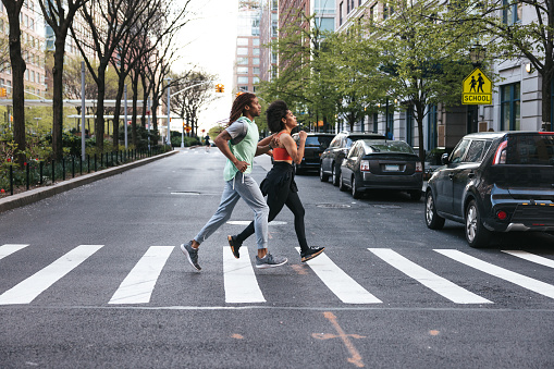 Sporty young couple running in the city of New York in the evening. Health and wellbeing concept, happy afro-american woman and man getting fit outdoors.