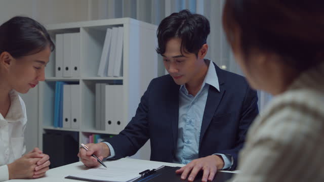 Young Asian businessman mentor corporate leader manager counselor communicate with businesswoman and sign a contract at office night. Businesspeople in workplace.