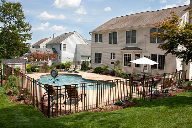 Lush backyard pool and patio behind colonial style home. Lush, resort-like backyard salt water swimming pool with flagstone stamped concrete patio behind colonial style home.  Bronze fencing is seen around the pool area of this suburban backyard. fence stock pictures, royalty-free photos & images