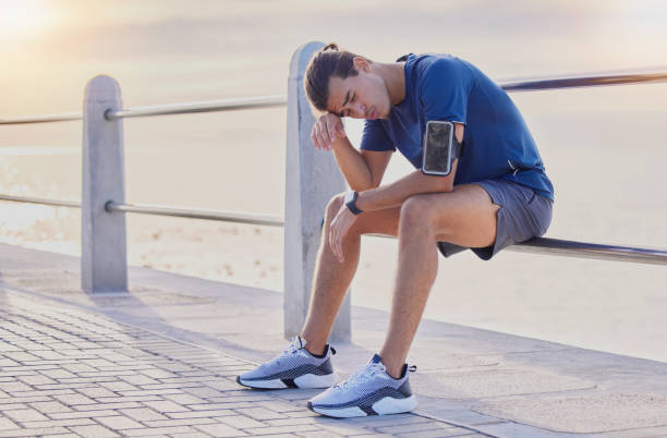 istock Tired runner man, sitting and beach for workout, health and exercise with headache, rest and relax. Gen z guy, training burnout and challenge with breathing, mindset and fitness on railing by ocean 1494780902