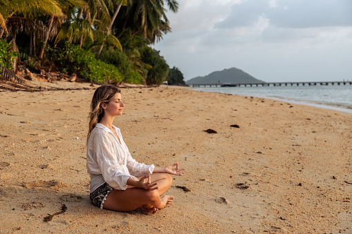 Woman exercising yoga at sunrise on the beach