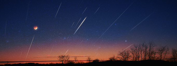 Silhouette of a countryside with Milky Way starry skies, meteor shower and crescent Moon.