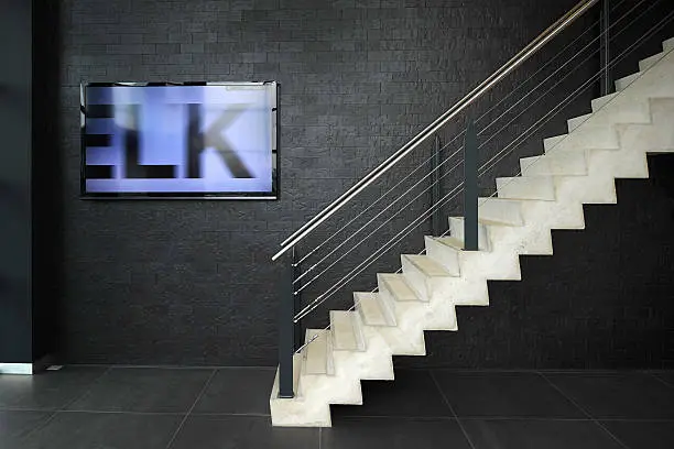 Stairs and a monitor showing  a welcome message for visitors  in the hall of an office building in The Netherlands. Current text on the monitor is "ELK", part of the Dutch word "WELKOM" ("Welcome" in English)
