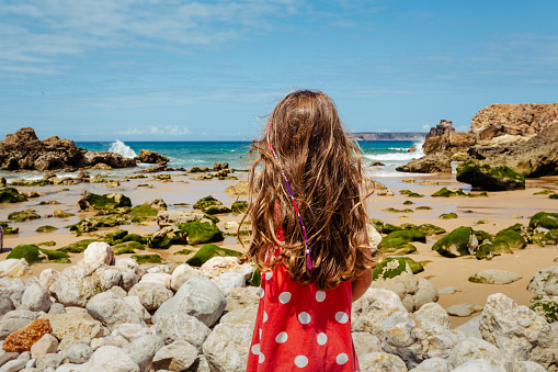 Little girl standing by the ocean a looking at the view. Photo taken in Algarve Portugal