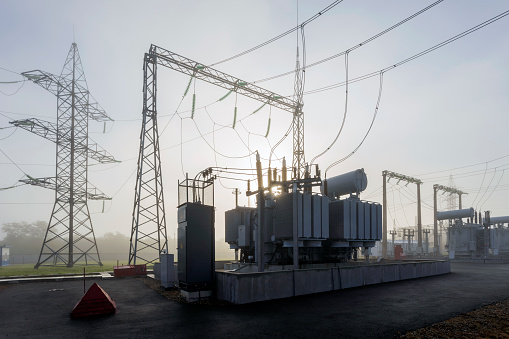 A high-voltage transformer illuminated in the fog by the sun.\nIndustrial substation in the fog in spring.