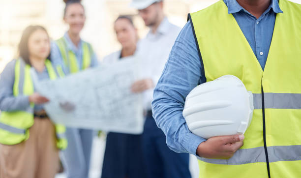 istock Helmet, construction and an architect standing on a building site with his team planning in the background. Leadership, architecture and renovation with an engineer holding a hard hat for maintenance 1494798115