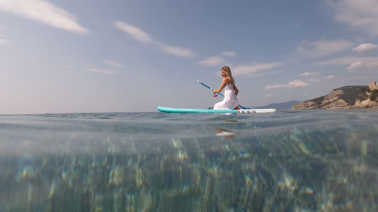 Young woman paddles board in white dress