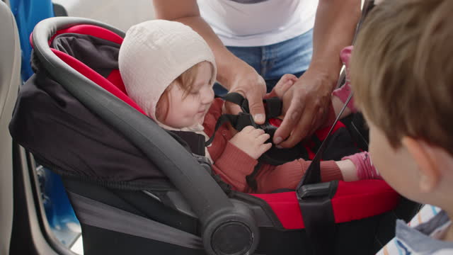 Father fastening safety belts of a baby car seat