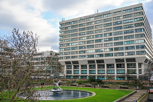 London, United Kingdom - February 02, 2019: St Thomas hospital building wall near London Bridge, green lawn with fountain in foreground. It is academic health science centre and teaching hospital